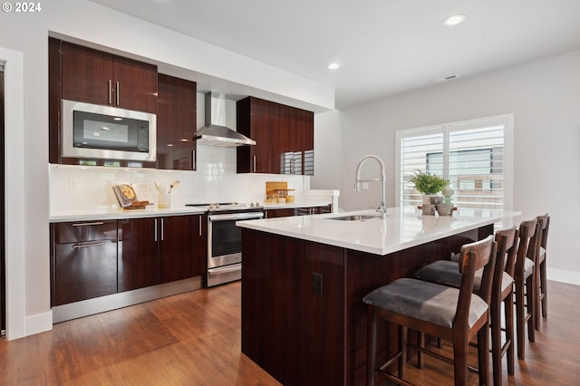 kitchen featuring wall chimney range hood, tasteful backsplash, sink, stainless steel appliances, and hardwood / wood-style flooring