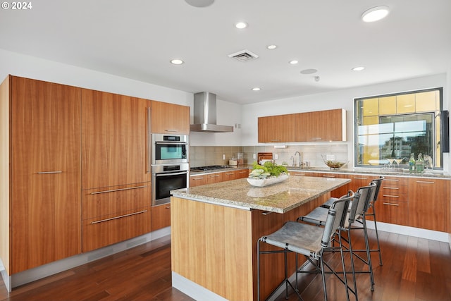 kitchen featuring a kitchen island, sink, a kitchen bar, stainless steel appliances, and wall chimney range hood