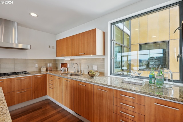 kitchen featuring wall chimney exhaust hood, sink, black gas cooktop, light stone countertops, and decorative backsplash