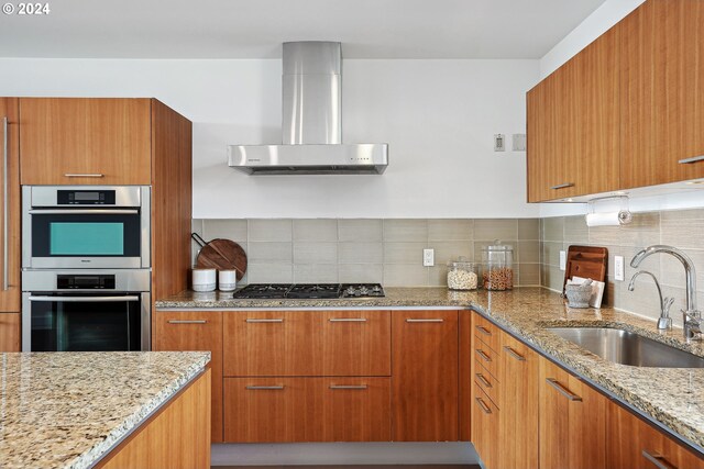 kitchen with wall chimney exhaust hood, sink, gas cooktop, stainless steel double oven, and light stone countertops