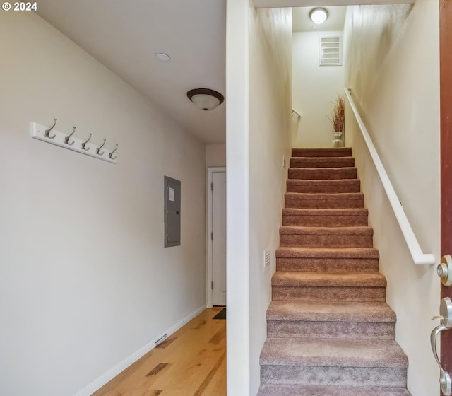 staircase with electric panel and hardwood / wood-style floors