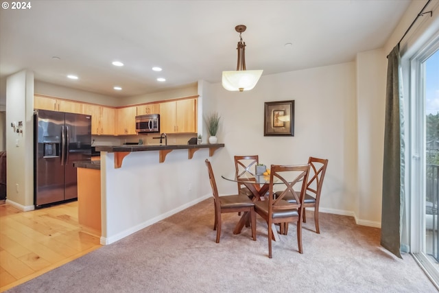 kitchen with a kitchen bar, decorative light fixtures, light brown cabinets, kitchen peninsula, and stainless steel appliances