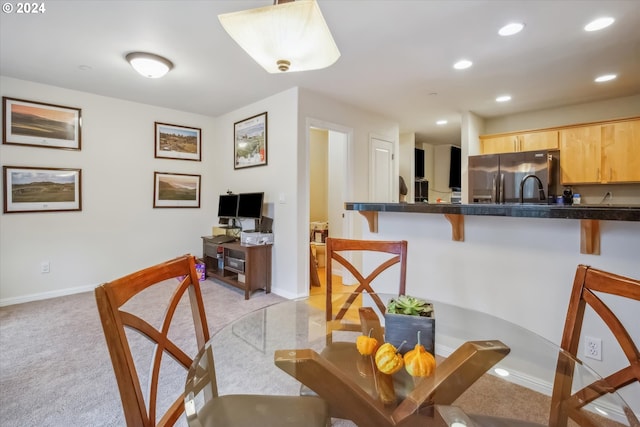 kitchen featuring a breakfast bar area, stainless steel refrigerator with ice dispenser, light colored carpet, kitchen peninsula, and light brown cabinets