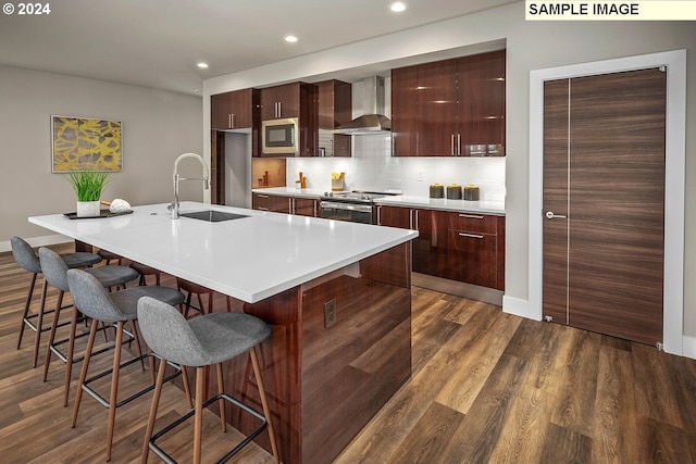 kitchen with sink, wall chimney exhaust hood, a breakfast bar area, a kitchen island with sink, and dark hardwood / wood-style flooring