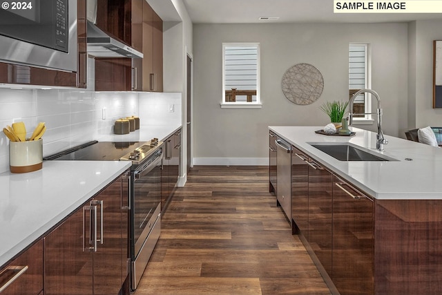 kitchen with stainless steel appliances, backsplash, sink, dark wood-type flooring, and wall chimney exhaust hood