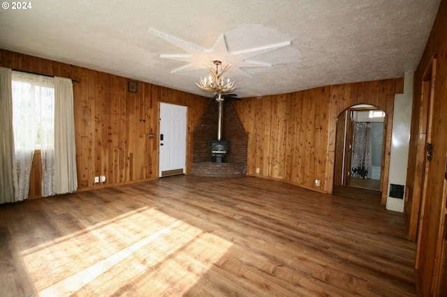 unfurnished living room featuring a wood stove, wood-type flooring, a textured ceiling, and wooden walls