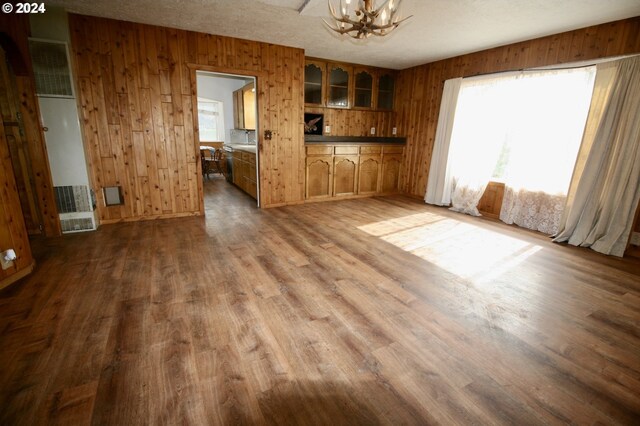 unfurnished living room with a notable chandelier, wood walls, hardwood / wood-style floors, and a textured ceiling