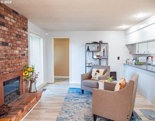 sitting room with brick wall, light hardwood / wood-style flooring, a brick fireplace, and a textured ceiling