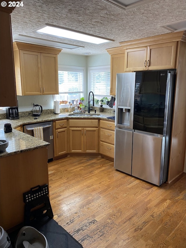 kitchen featuring stainless steel appliances, sink, light hardwood / wood-style flooring, light brown cabinetry, and a textured ceiling