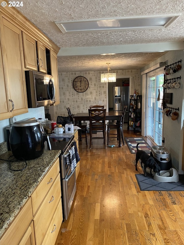 kitchen featuring light brown cabinets, wood-type flooring, appliances with stainless steel finishes, stone counters, and a textured ceiling