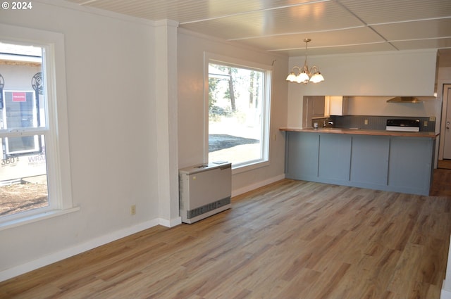705 Couch Ave, Wallowa, OR 97885 - kitchen with heating unit, a chandelier, wall chimney range hood, light wood finished floors, and baseboards