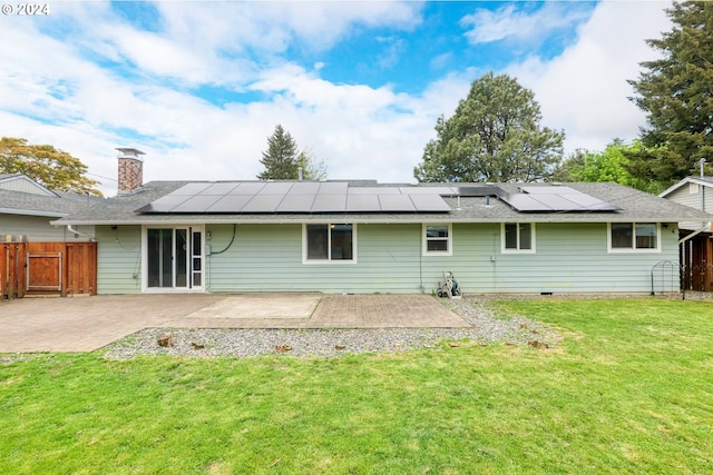 rear view of house with solar panels, a patio area, and a lawn