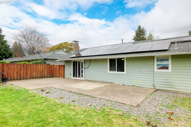 back of house with solar panels, a patio area, and a lawn