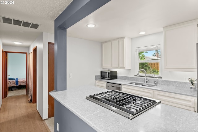 kitchen with light stone countertops, white cabinetry, stainless steel appliances, sink, and light hardwood / wood-style floors