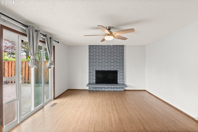 unfurnished living room featuring ceiling fan, a brick fireplace, a textured ceiling, light hardwood / wood-style floors, and brick wall