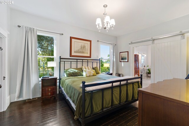 bedroom featuring dark wood-style floors, a barn door, and an inviting chandelier