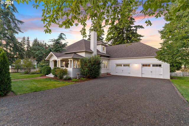 view of front facade featuring aphalt driveway, a chimney, a shingled roof, a front yard, and a garage