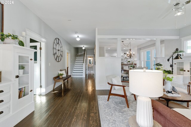 living area with dark wood-style floors, stairs, baseboards, and an inviting chandelier