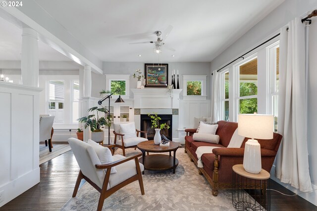 living area featuring wood finished floors, plenty of natural light, a fireplace, and decorative columns