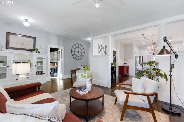 living area with decorative columns, a decorative wall, wood finished floors, and wainscoting