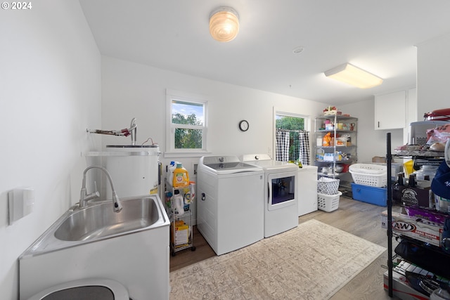 laundry area featuring strapped water heater, separate washer and dryer, light hardwood / wood-style flooring, and sink