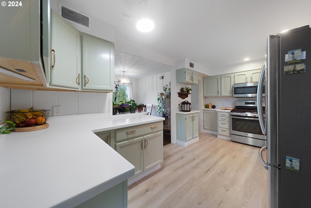 kitchen featuring kitchen peninsula, stainless steel appliances, decorative light fixtures, and light hardwood / wood-style floors