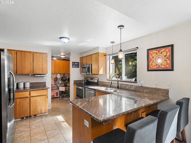 kitchen featuring pendant lighting, dark stone counters, light tile patterned flooring, kitchen peninsula, and stainless steel appliances