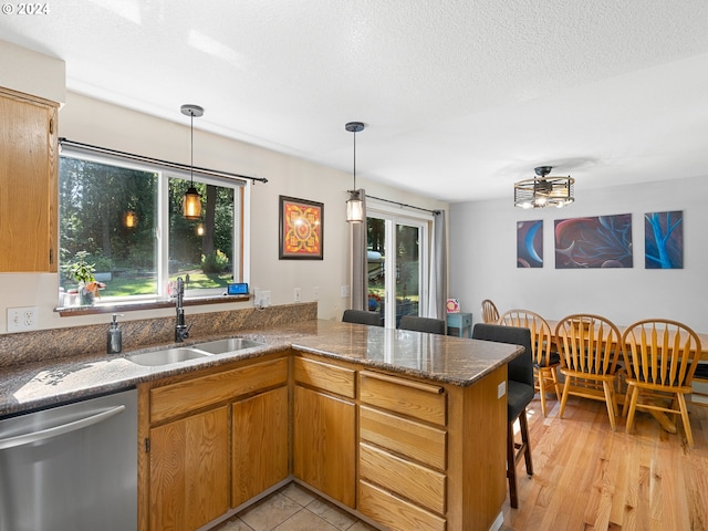 kitchen with stainless steel dishwasher, kitchen peninsula, sink, and a wealth of natural light