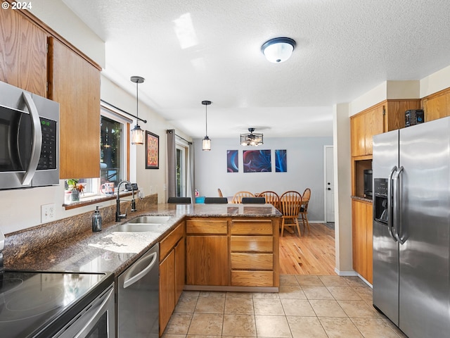 kitchen with sink, light tile patterned floors, decorative light fixtures, kitchen peninsula, and stainless steel appliances