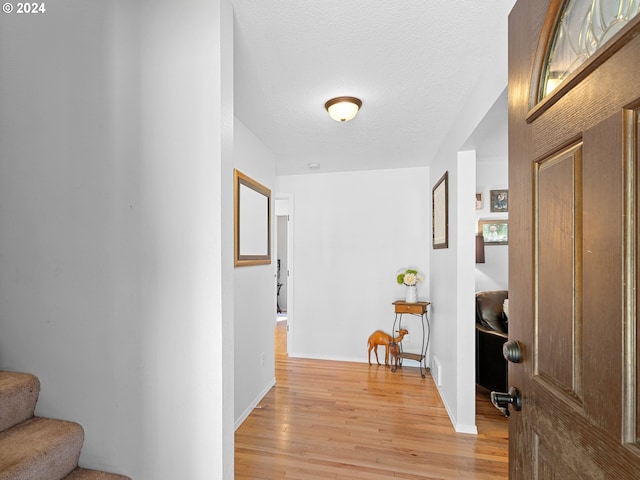 hall with light hardwood / wood-style floors and a textured ceiling