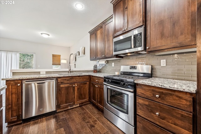 kitchen with light stone countertops, appliances with stainless steel finishes, dark hardwood / wood-style flooring, kitchen peninsula, and sink