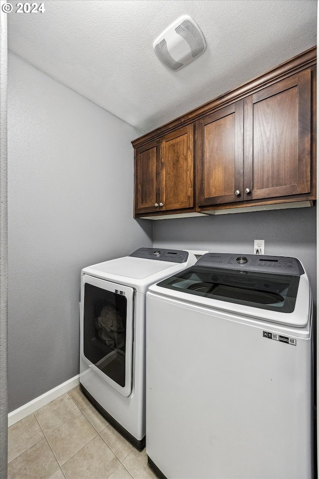 laundry room with washer and dryer, light tile patterned floors, a textured ceiling, and cabinets