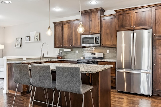 kitchen with hanging light fixtures, a kitchen breakfast bar, light stone counters, dark hardwood / wood-style floors, and appliances with stainless steel finishes