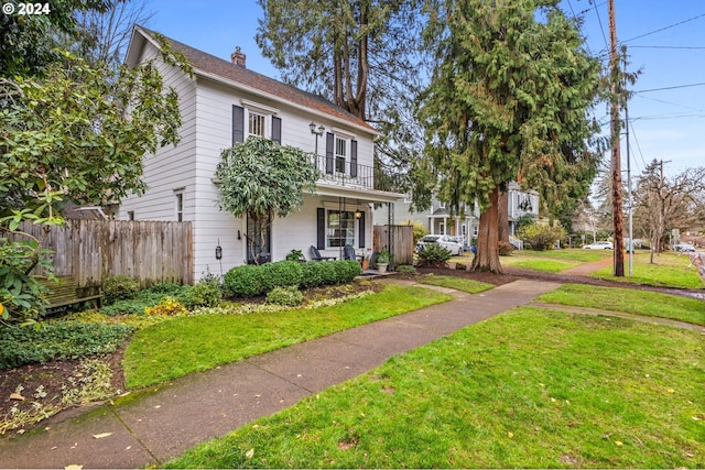 view of front of house with a porch, a balcony, and a front lawn