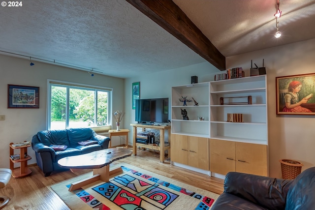 living room featuring beamed ceiling, light wood-type flooring, and a textured ceiling