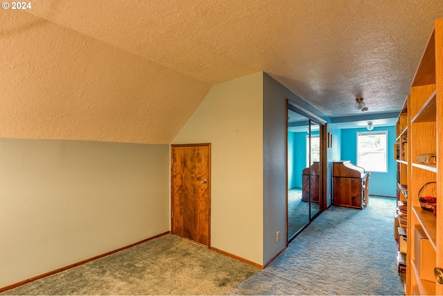 corridor featuring carpet, vaulted ceiling, and a textured ceiling