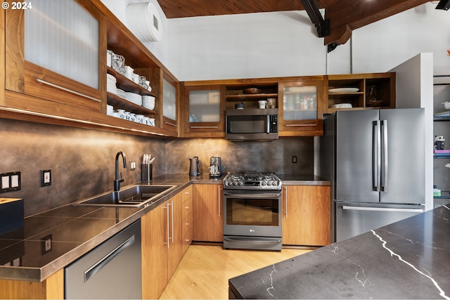 kitchen with sink, light hardwood / wood-style flooring, decorative backsplash, appliances with stainless steel finishes, and beam ceiling