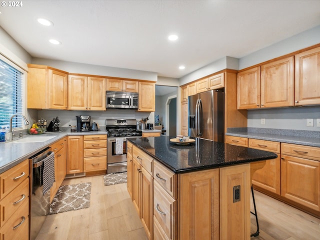 kitchen featuring appliances with stainless steel finishes, sink, a kitchen island, dark stone countertops, and light hardwood / wood-style flooring