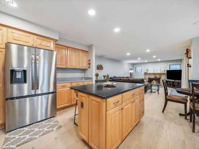 kitchen featuring light brown cabinets, stainless steel fridge with ice dispenser, dark stone countertops, light hardwood / wood-style floors, and a center island