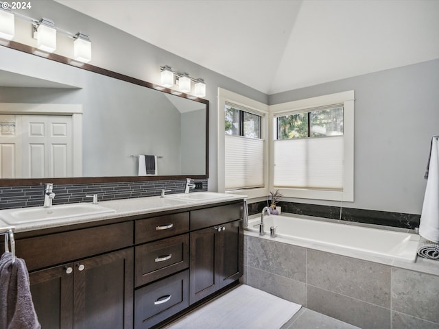 bathroom featuring vanity, lofted ceiling, backsplash, and tiled bath