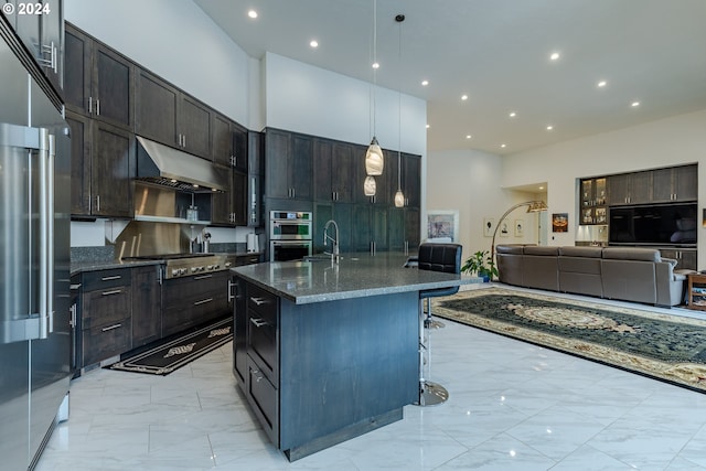 kitchen with dark stone counters, stainless steel appliances, decorative light fixtures, a center island with sink, and a breakfast bar area