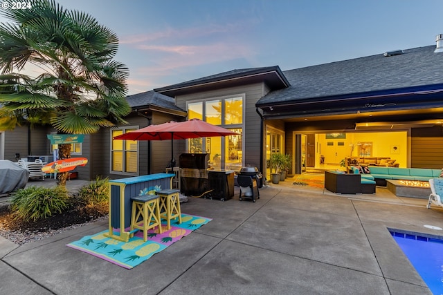 back house at dusk with outdoor lounge area, a patio area, and a bar