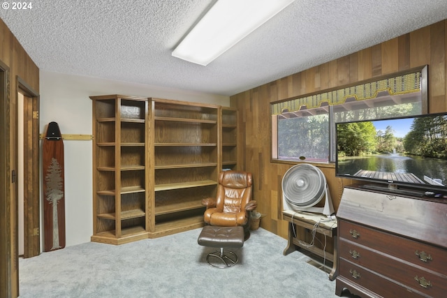 sitting room with light carpet, a textured ceiling, and wooden walls