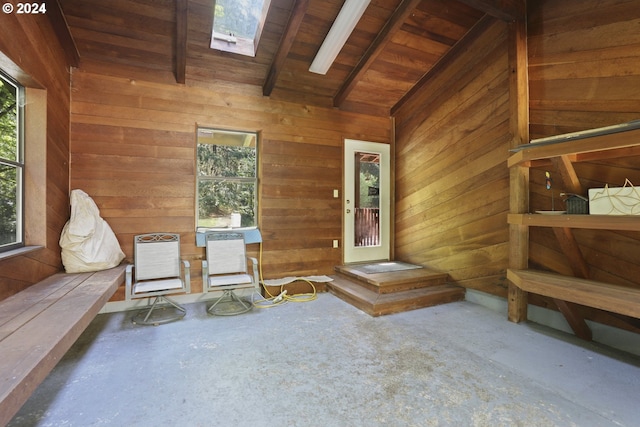 interior space with lofted ceiling with skylight, wooden walls, concrete flooring, and a wealth of natural light