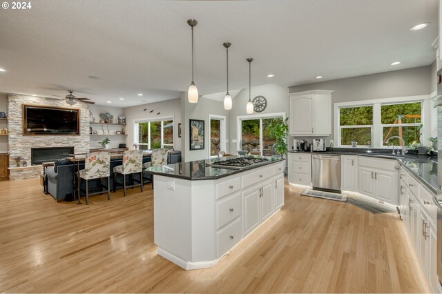 kitchen with appliances with stainless steel finishes, white cabinetry, a fireplace, a kitchen island, and decorative light fixtures