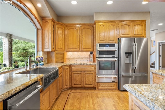 kitchen with appliances with stainless steel finishes, light hardwood / wood-style flooring, sink, decorative backsplash, and light stone countertops