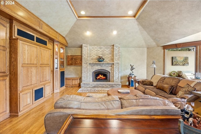 living room featuring a textured ceiling, light hardwood / wood-style flooring, a brick fireplace, and vaulted ceiling