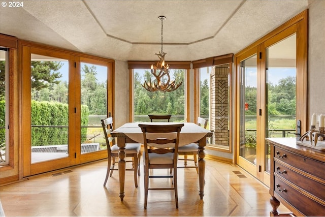 sunroom featuring a wealth of natural light, a raised ceiling, and a chandelier