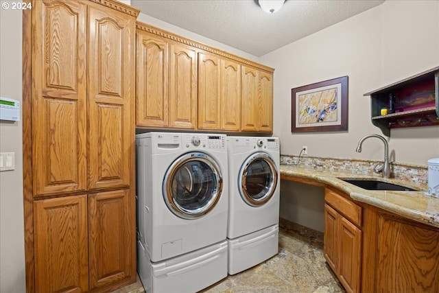 clothes washing area featuring washing machine and clothes dryer, sink, cabinets, a textured ceiling, and light tile patterned flooring