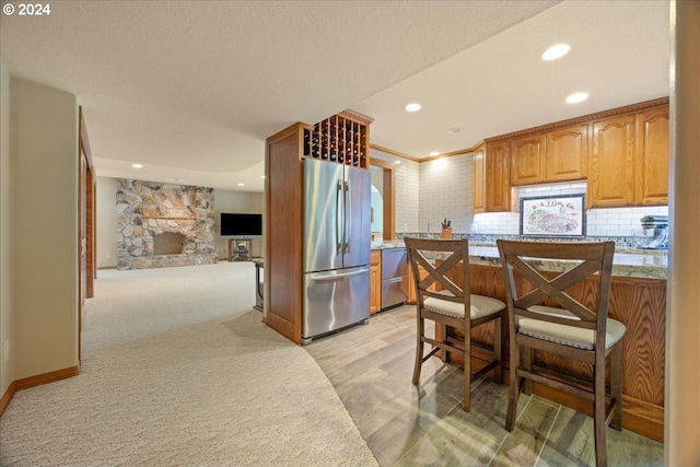 kitchen with a fireplace, light colored carpet, backsplash, and stainless steel appliances